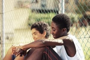 Teenage boys sitting together against a fence in the summertime, a benefit of social skills training in Toronto.
