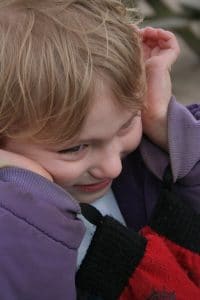 Child with sensory processing disorder covering ears and smiling while playing outside. 
