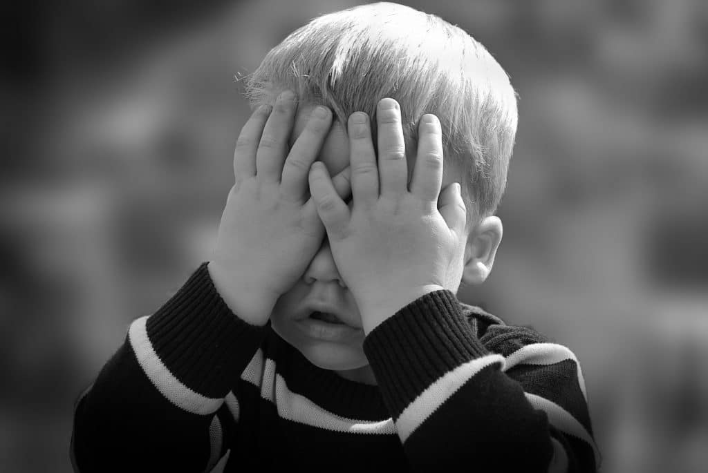 Toddler boy covering his eyes. Lack of eye contact is a red flag for autism. 