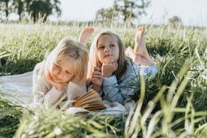 Two girls laying in the grass, reading and talking using autoclitics in their language. 